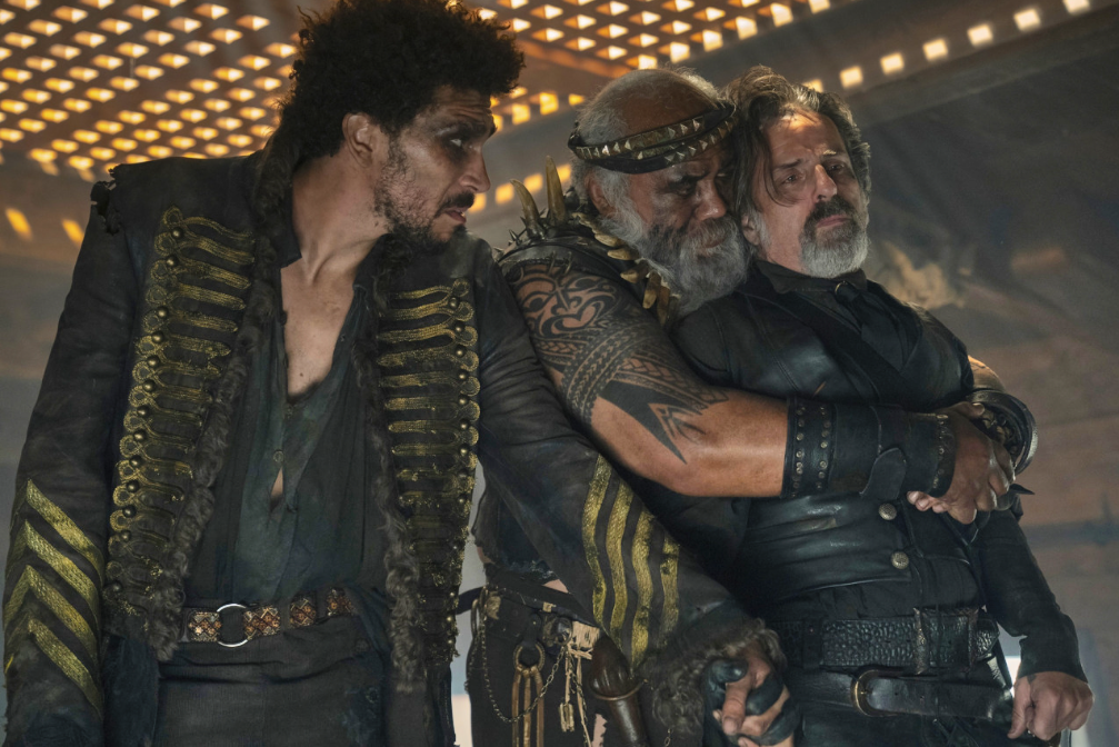 A still from s02e01 of Our Flag Means Death in which Izzy Hands is being bear-hugged from behind by Fang while Frenchie holds his hand, fingers interlaced.