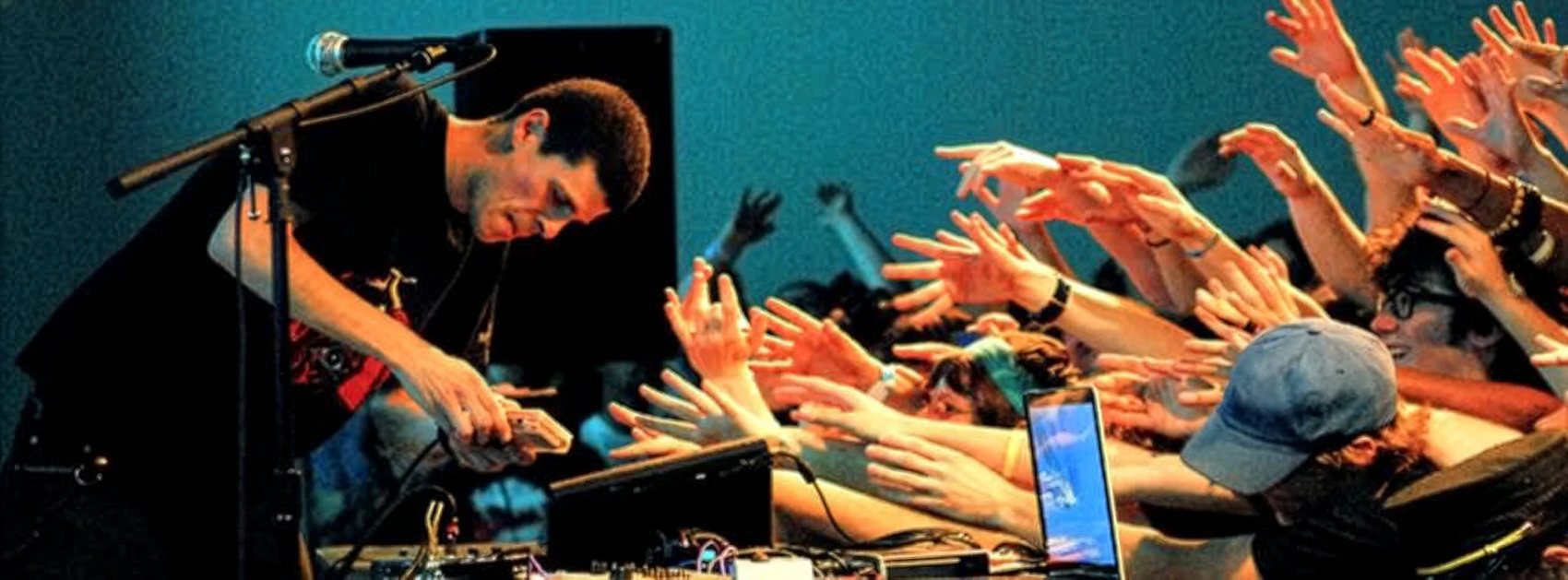 Mans del públic alçades cap a l'artista, que toca amb una Game Boy
