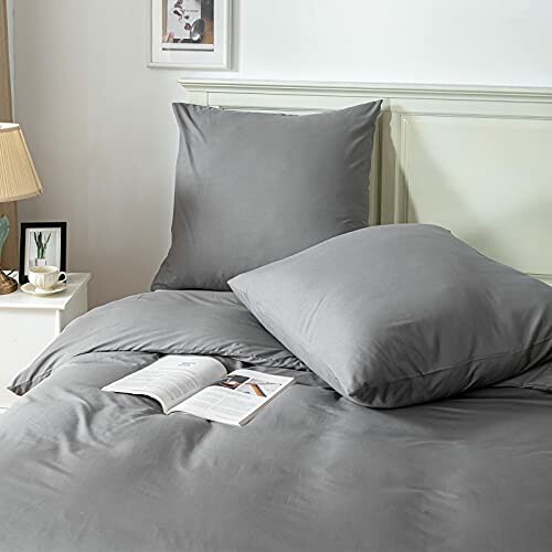 Graue Bettwäsche auf einem Bett mit Kissen und Buch.