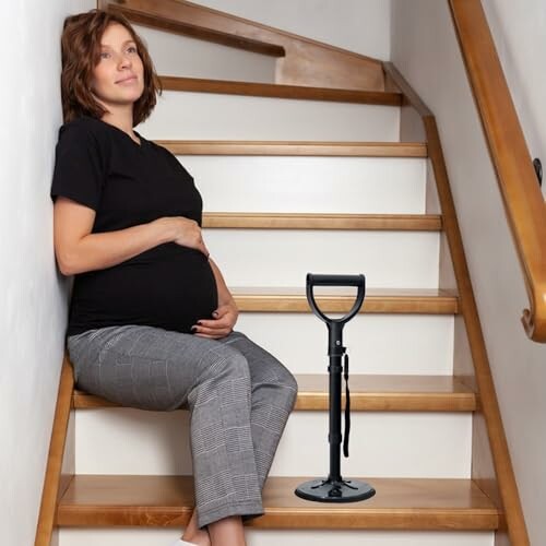 Schwangere Frau sitzt auf Treppe neben Haltegriff.